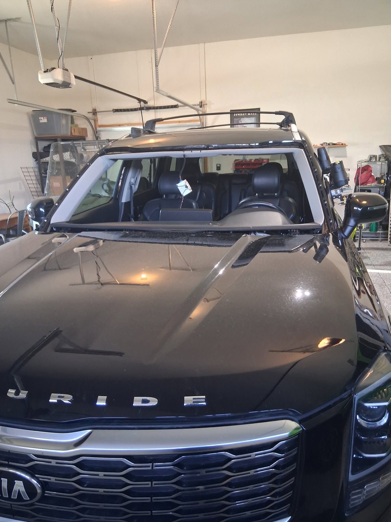 Black Kia SUV in a garage, front view with roof rack and hood lettering.