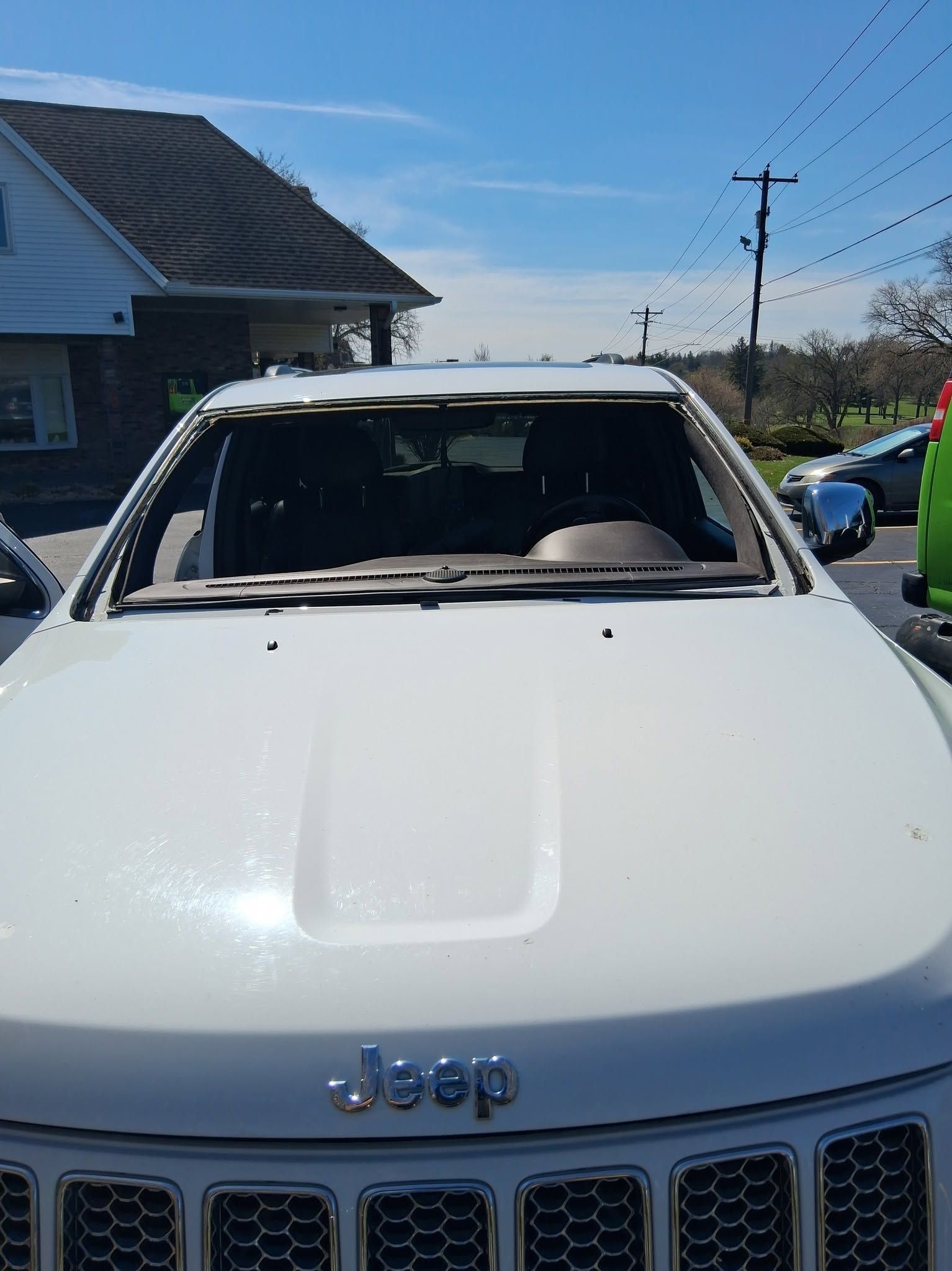 White Jeep with a shattered windshield parked outdoors on a sunny residential street
