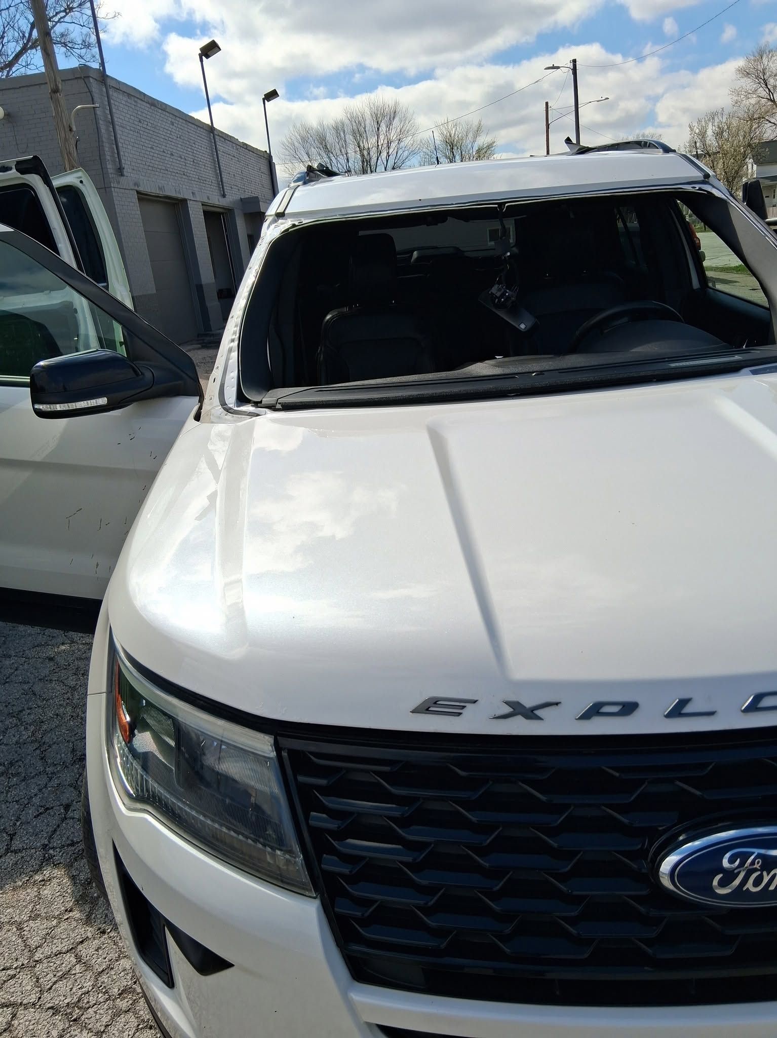 White Ford Explorer parked outdoors with a damaged windshield and open driver’s door