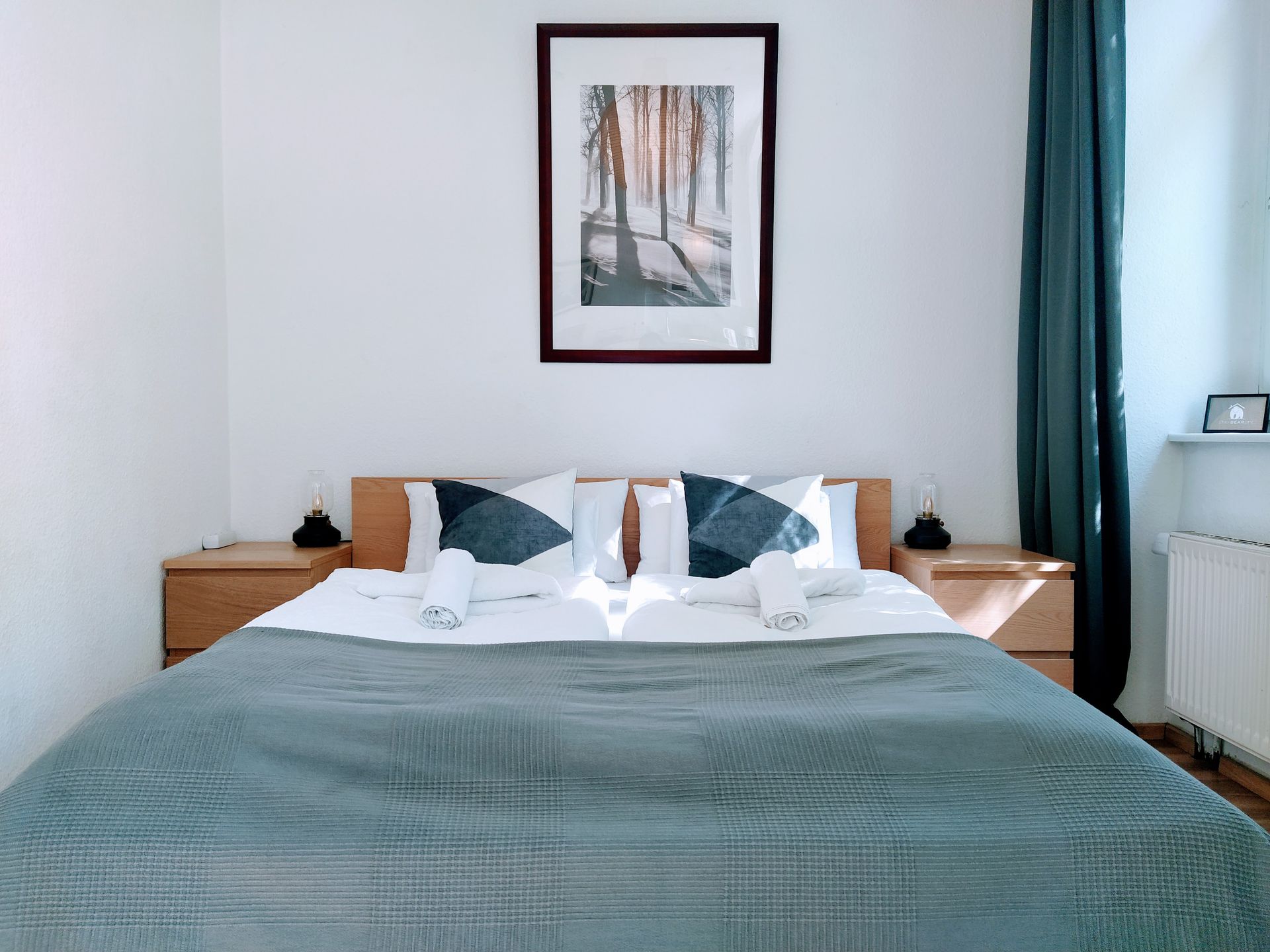 A bedroom with a bed , nightstands , and a picture on the wall above the bed in our holiday apartment in Berlin.