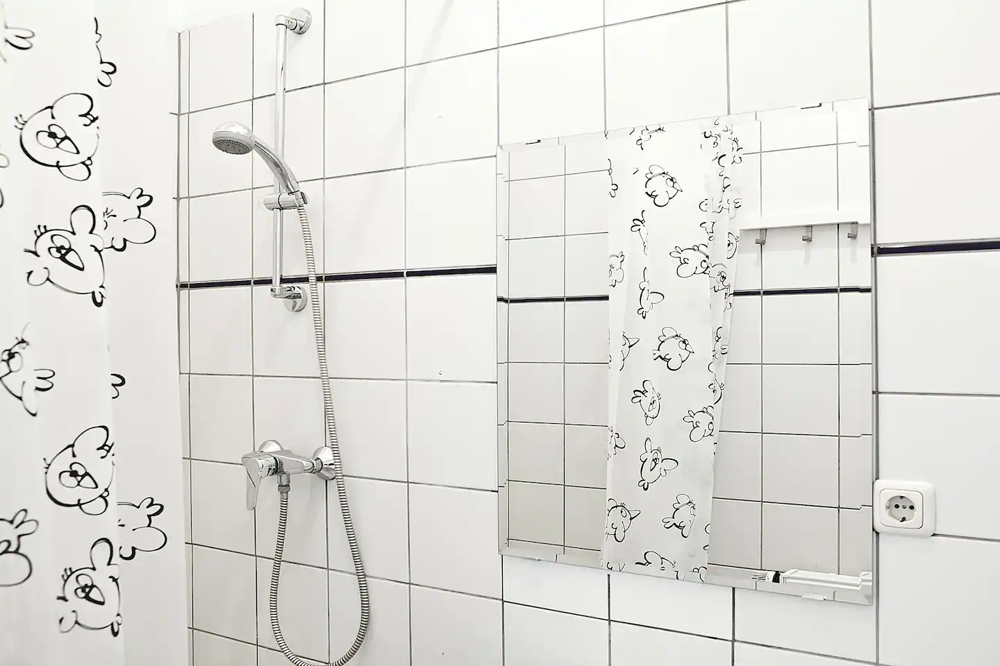 A bathroom with white tiles , a shower head and a mirror in our holiday apartment in Berlin.