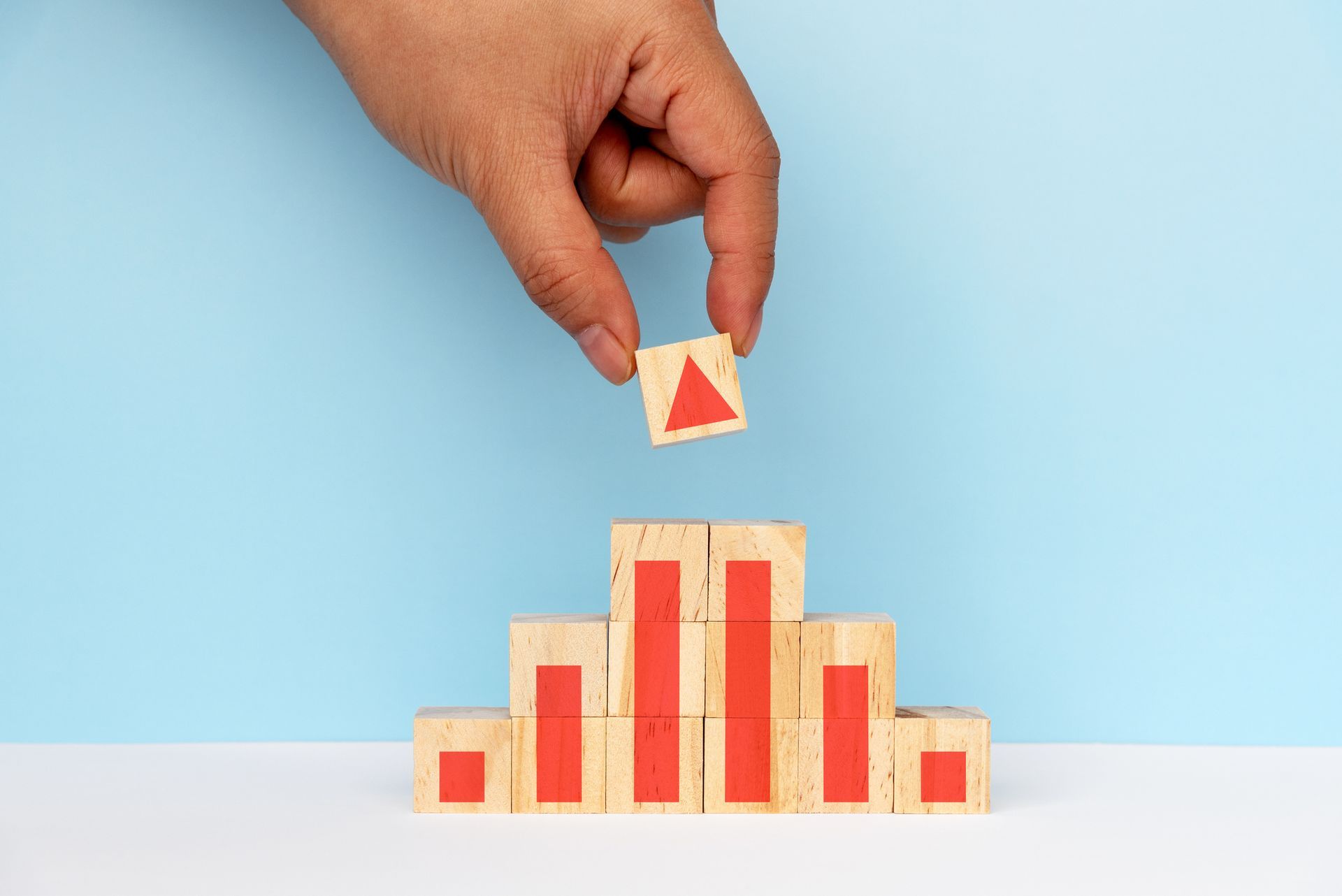 A hand is holding a wooden block with a red triangle on it.