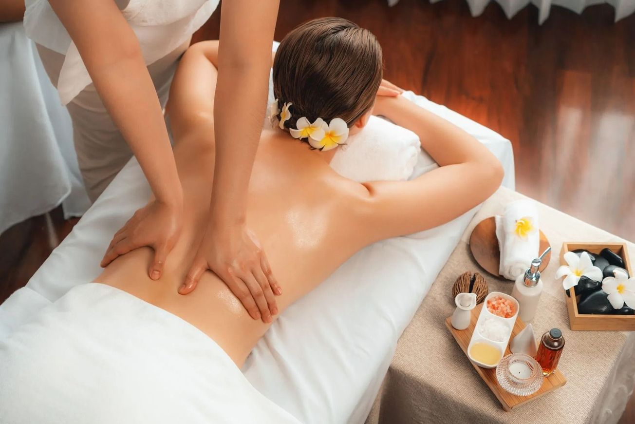 Masajista dando un masaje de espalda en una camilla de spa con velas y flores cerca.