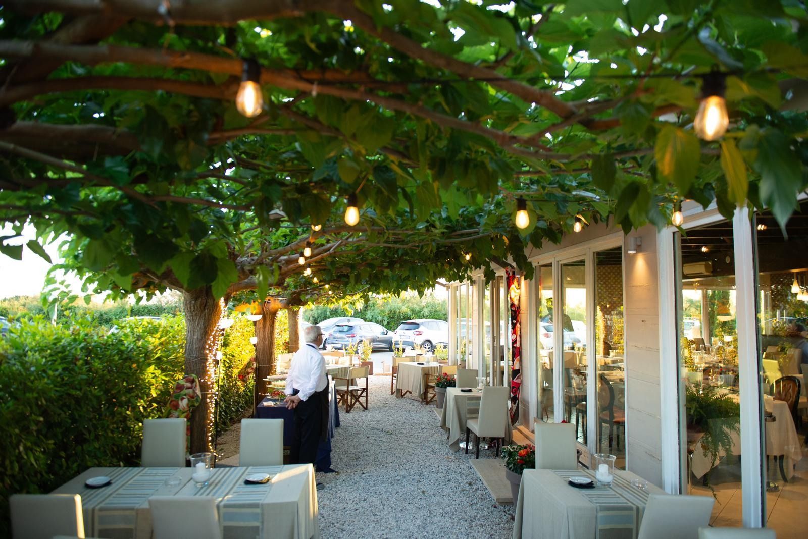 Terrazza esterna del ristorante con tavoli, luci decorative sotto una tettoia di foglie 