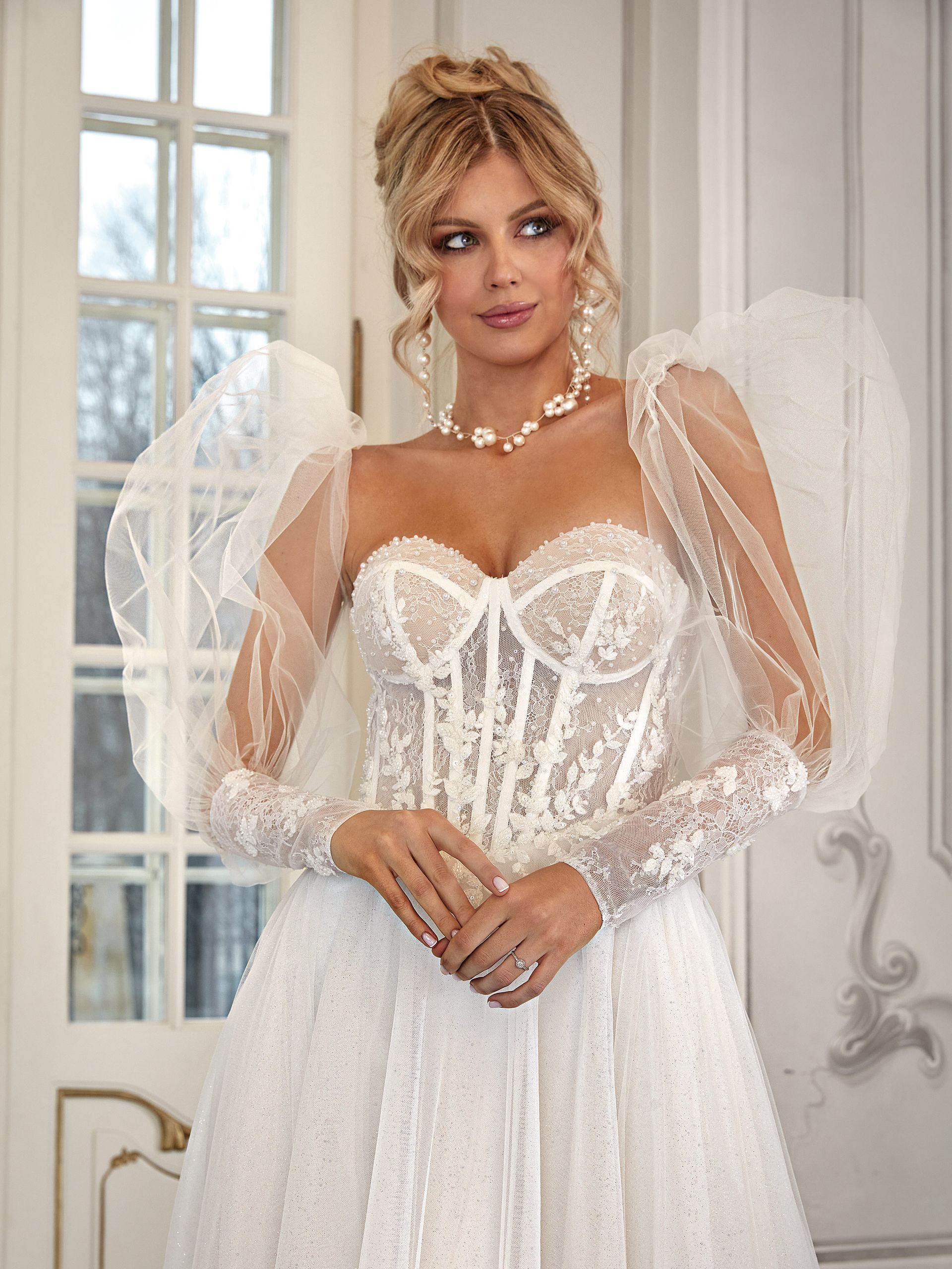 Eine Frau in einem weißen Brautkleid mit Puffärmeln steht vor einem Gebäude.