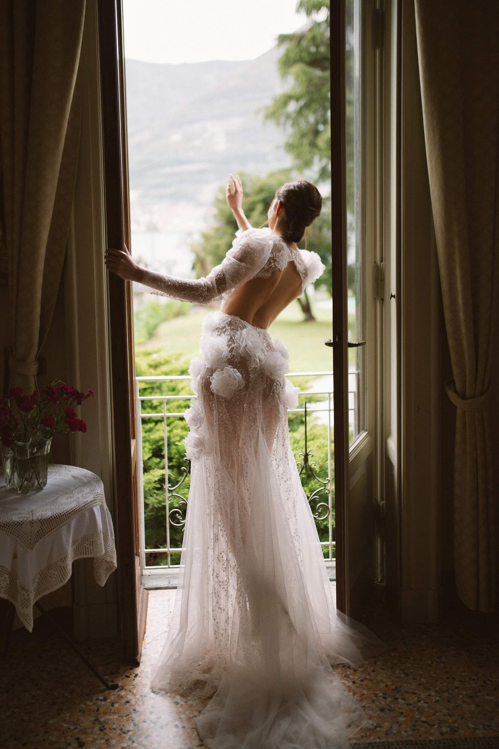 Eine Frau in einem Brautkleid steht vor einem Fenster.