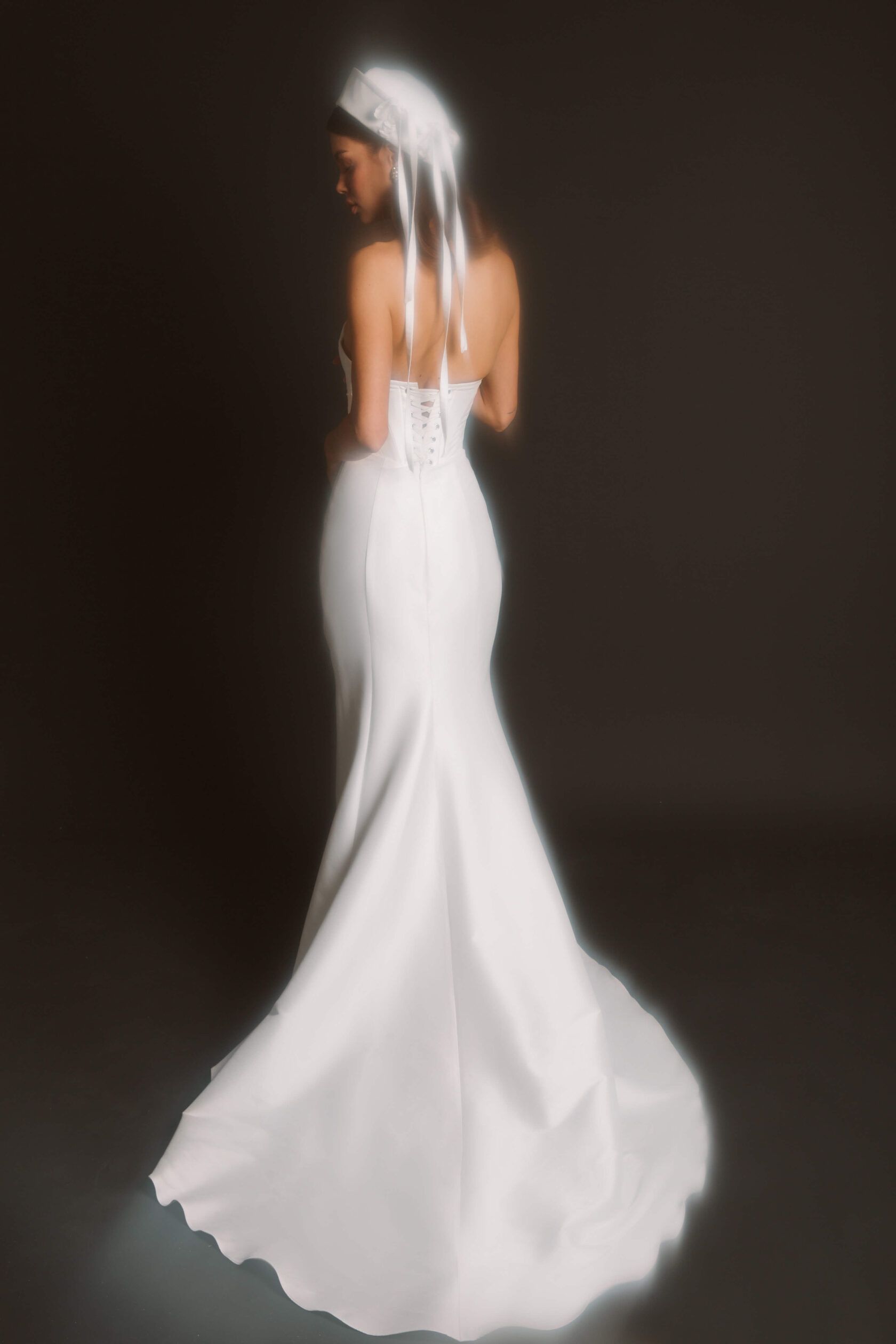 Eine Frau in einem weißen Brautkleid steht vor einem schwarzen Hintergrund.