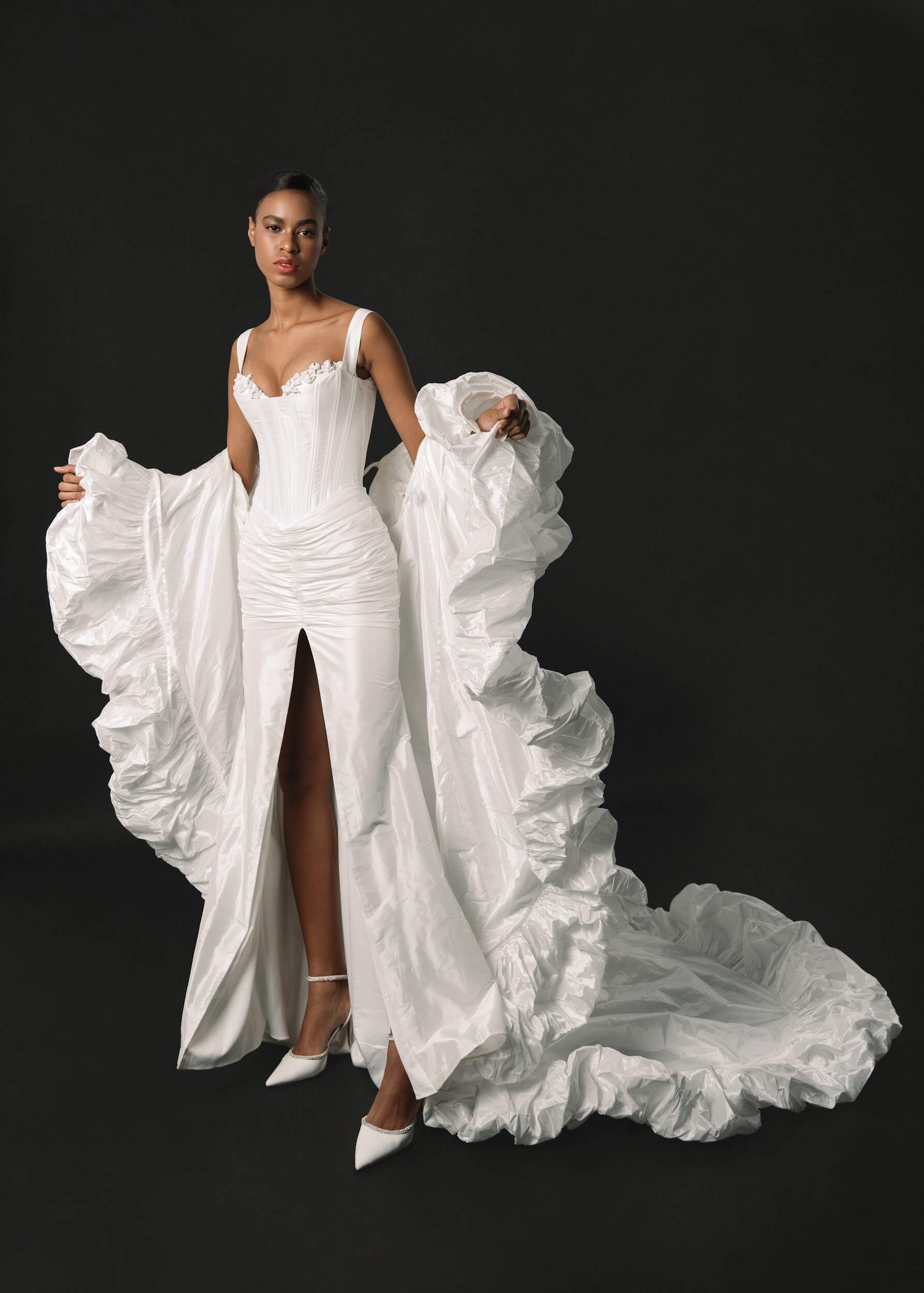 Eine Frau in einem weißen Brautkleid steht vor einem schwarzen Hintergrund.
