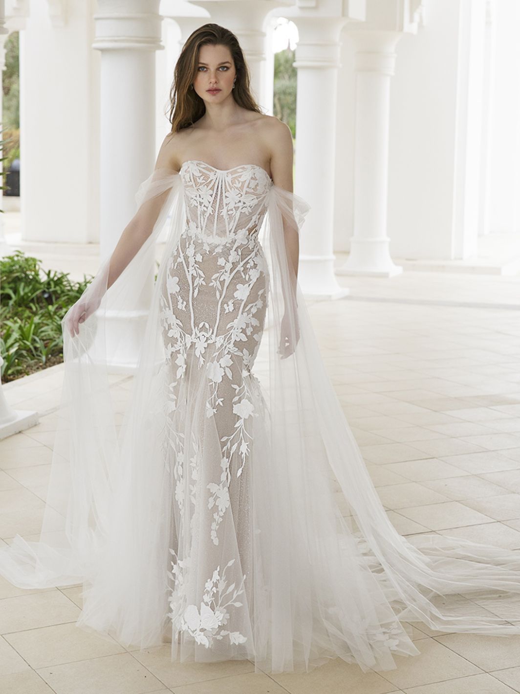 Eine Frau trägt ein Brautkleid mit Umhang und Handschuhen.