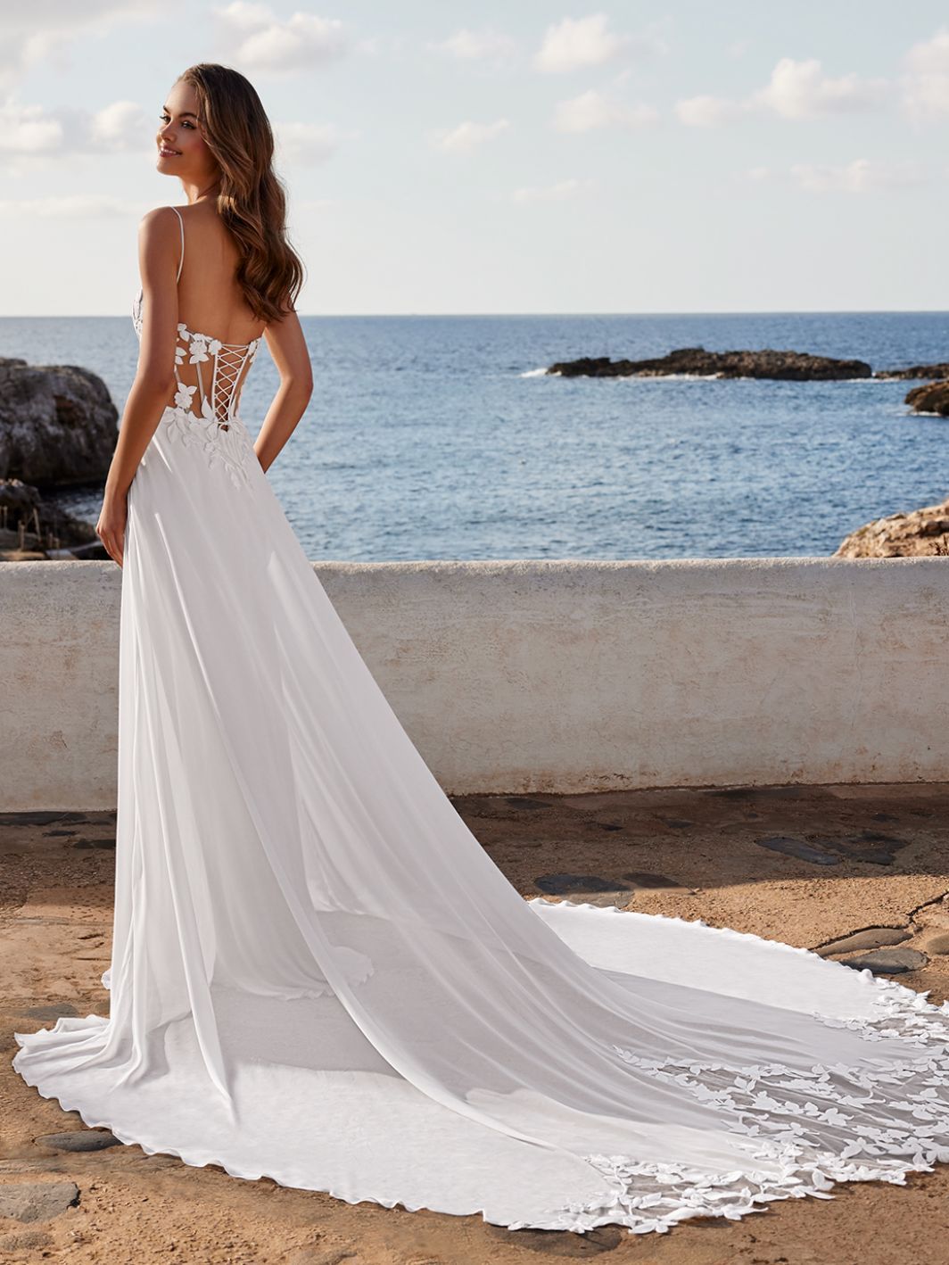 Eine Frau in einem weißen Brautkleid steht vor dem Meer.