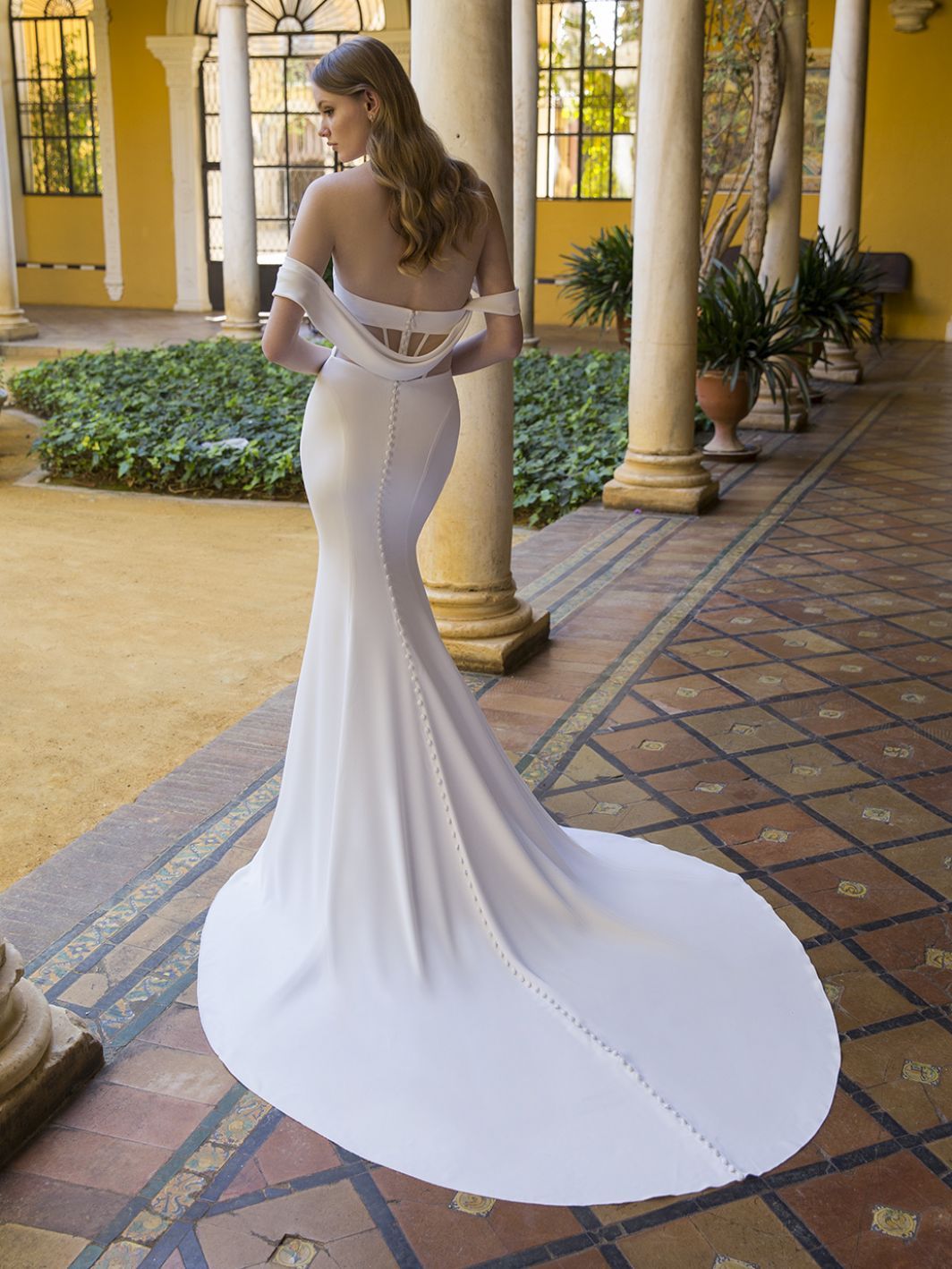 Eine Frau in einem weißen Brautkleid steht in einem Innenhof.