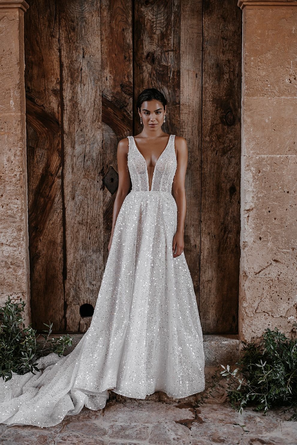 Eine Frau in einem weißen Brautkleid steht vor einer Holztür.
