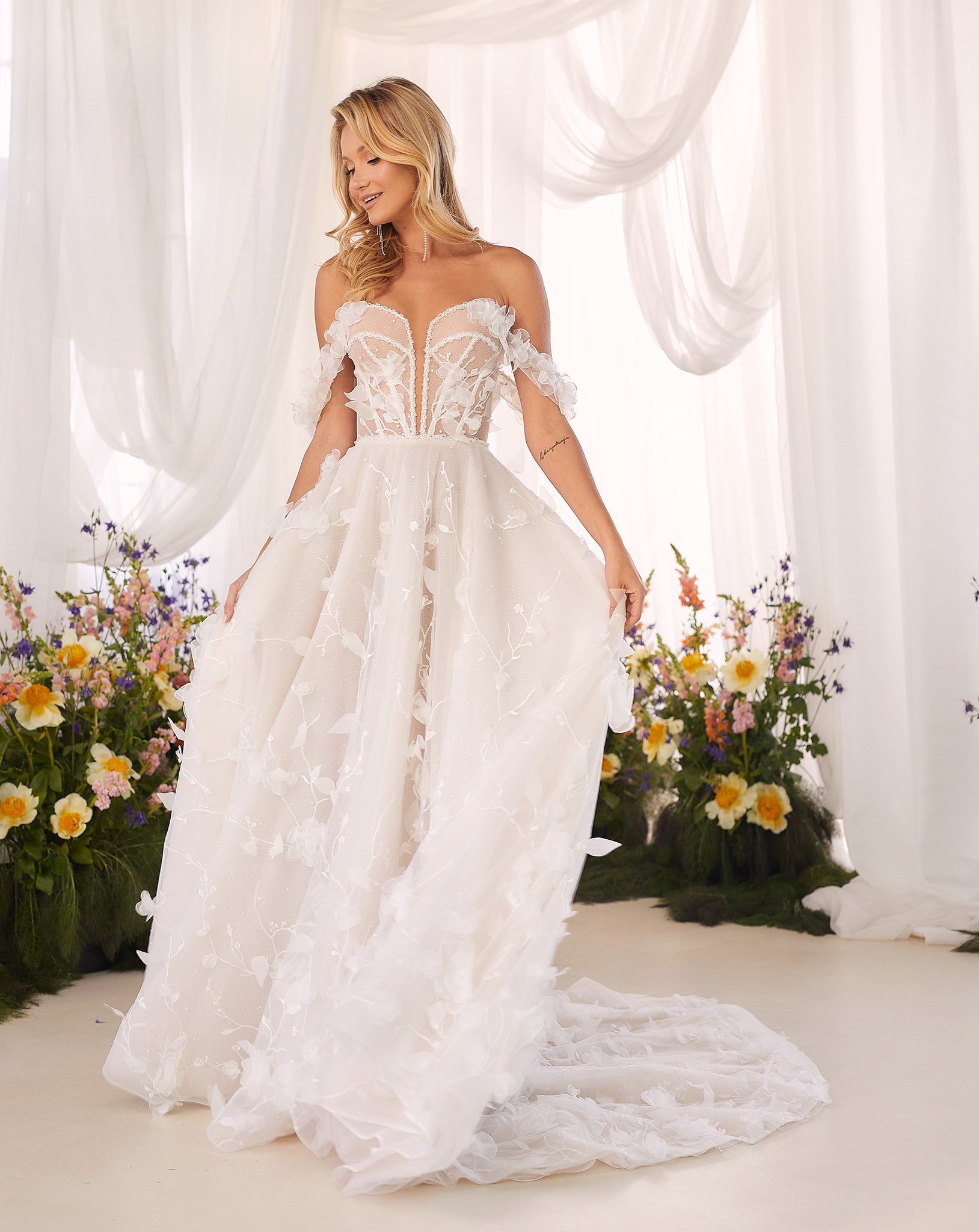 Eine Frau in einem weißen Brautkleid steht vor Blumen.