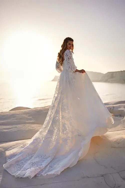 Eine Frau in einem weißen Spitzenbrautkleid steht an einem Strand.
