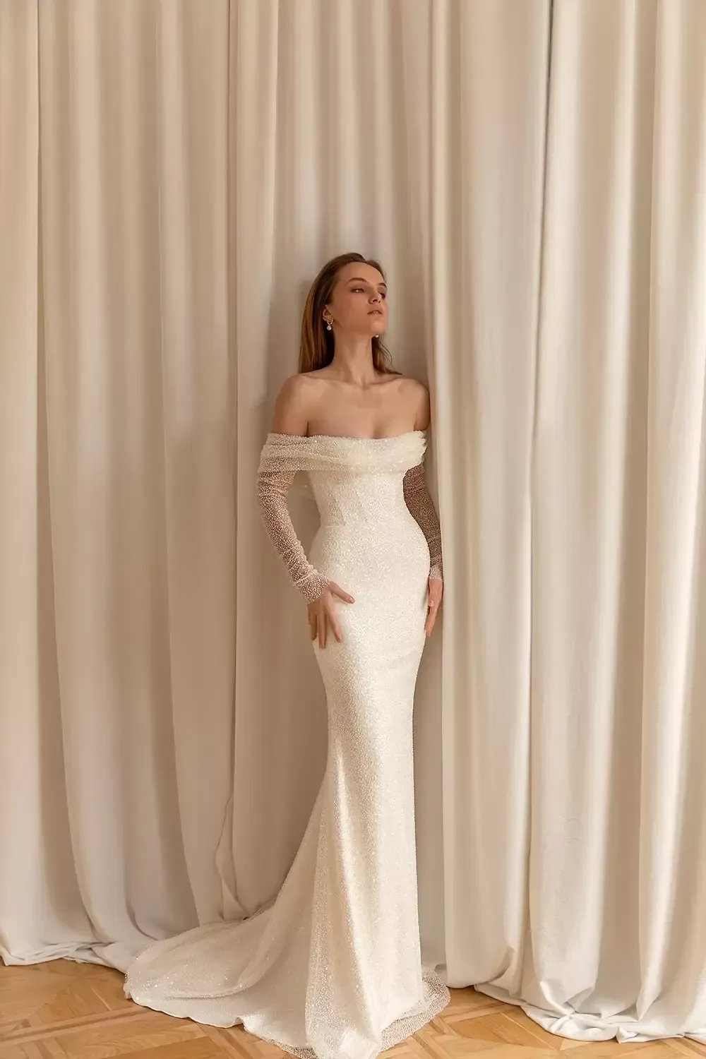 Eine Frau in einem Brautkleid steht vor einem weißen Vorhang.
