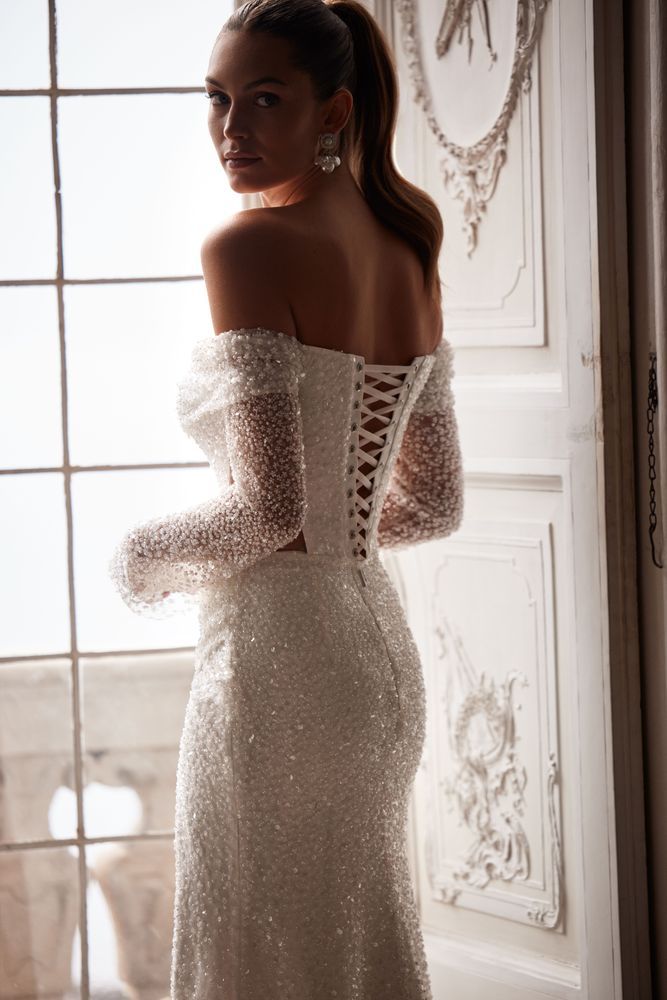 Eine Frau in einem Brautkleid steht vor einem Fenster.