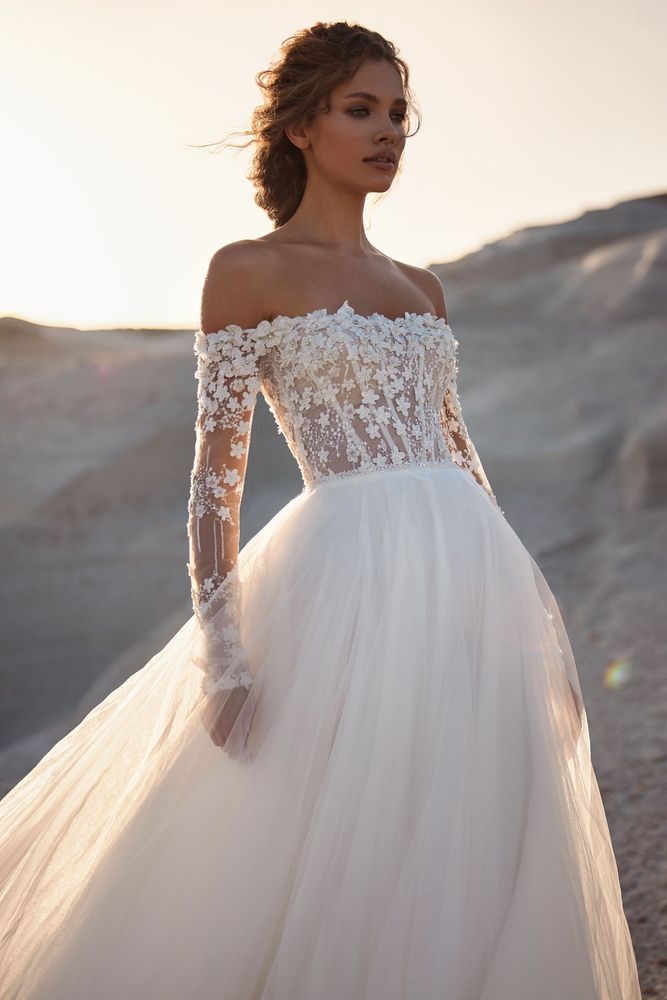 Eine Frau in einem weißen Brautkleid mit langen Ärmeln steht in der Wüste.