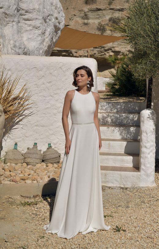 Eine Frau in einem weißen Brautkleid steht vor einem weißen Gebäude.
