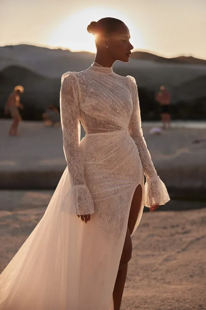 Eine Frau in einem weißen Spitzenkleid steht bei Sonnenuntergang an einem Strand.