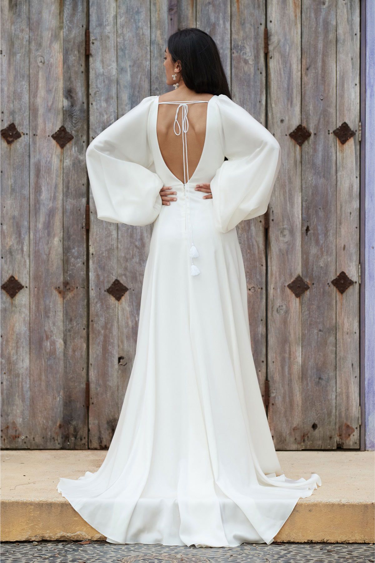 Eine Frau in einem weißen Kleid steht vor einer Holztür.
