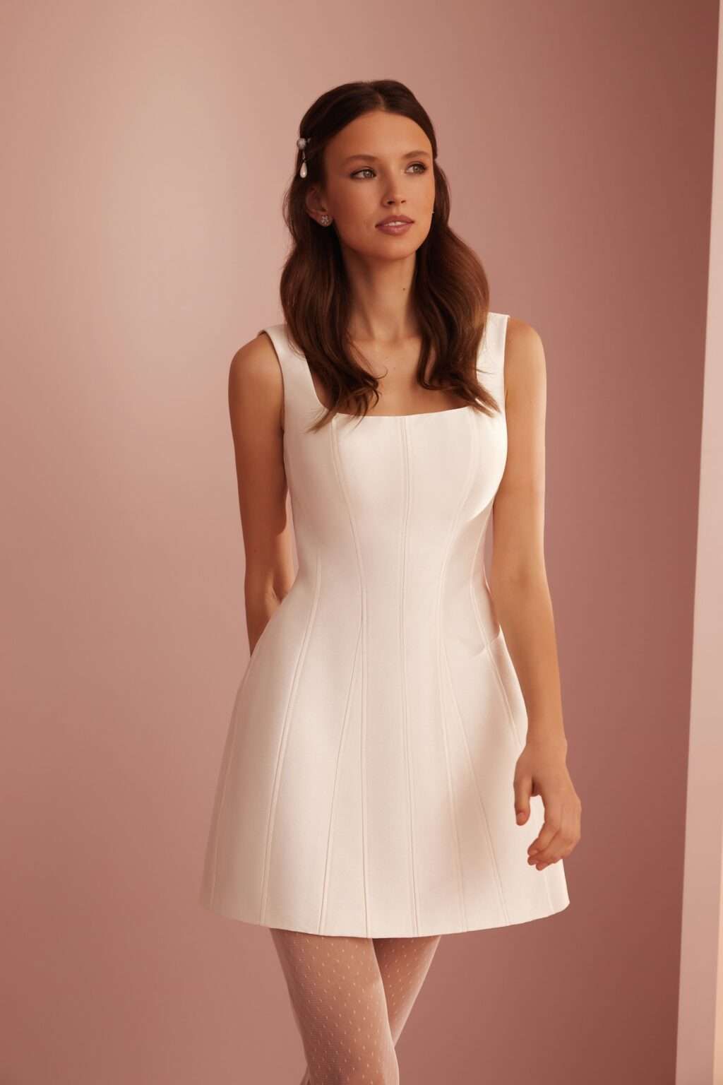 Eine Frau in einem weißen Kleid steht vor einer rosa Wand.