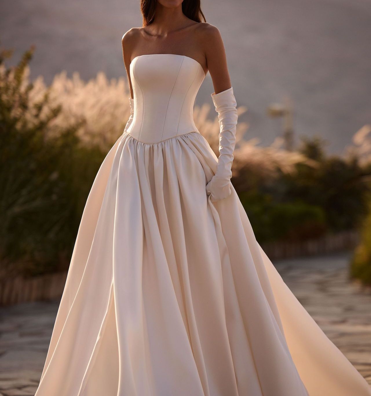 Frau in einem weißen trägerlosen Brautkleid mit langen Handschuhen, im Freien stehend.