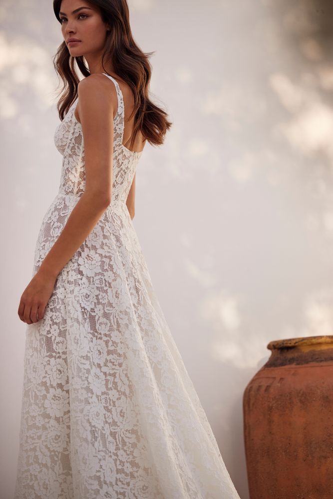 Eine Frau in einem weißen Spitzenbrautkleid steht neben einer Vase.