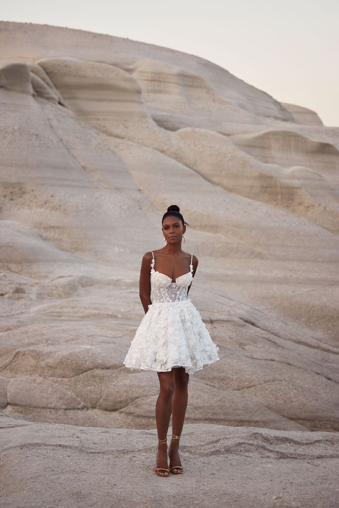 Eine Frau in einem kurzen weißen Kleid steht in der Wüste.