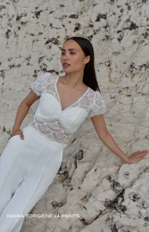 Eine Frau in einem weißen Spitzentop und einer weißen Hose steht im Sand.