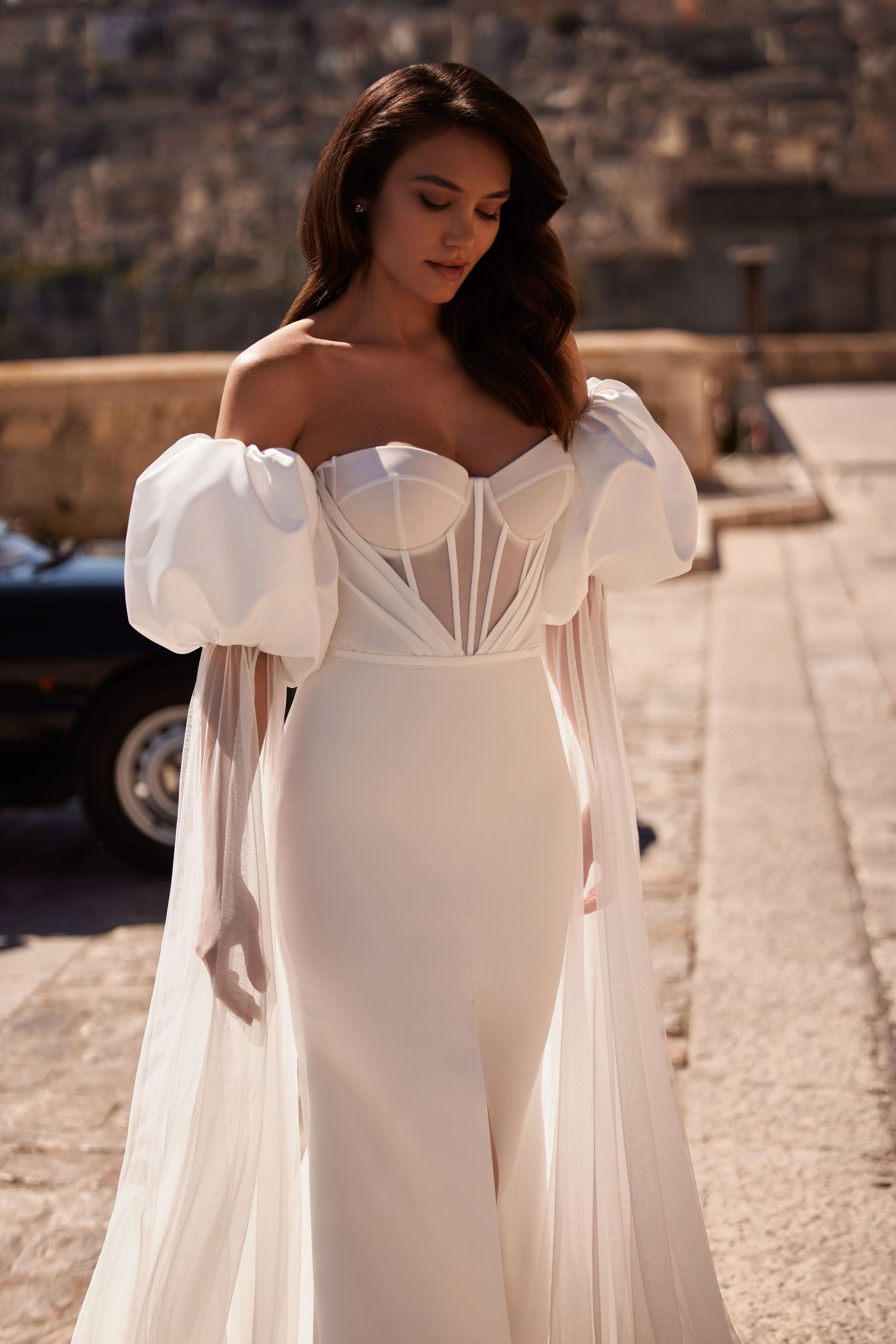 Eine Frau in einem weißen Brautkleid mit Puffärmeln steht auf einem Bürgersteig.