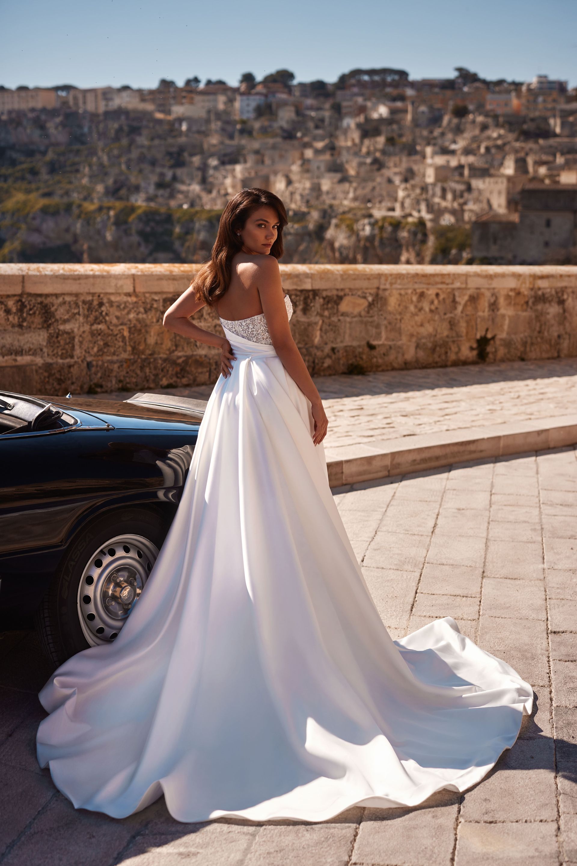 Eine Frau in einem weißen Brautkleid steht neben einem schwarzen Auto.