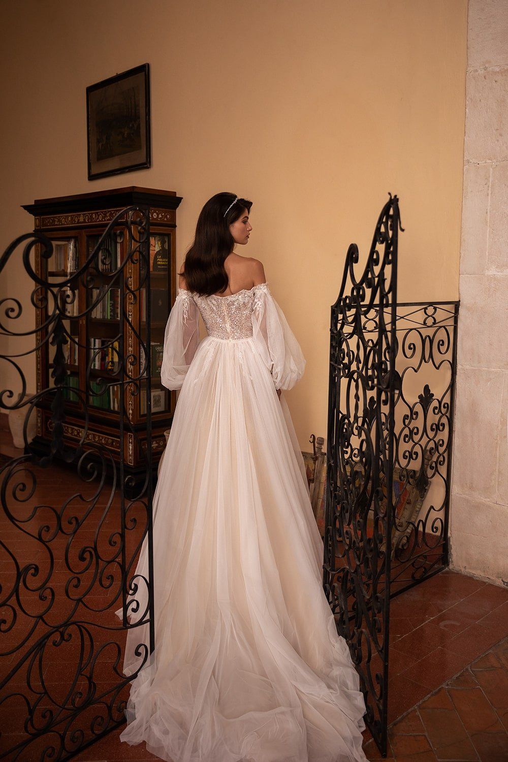 Eine Frau in einem Brautkleid steht neben einem schmiedeeisernen Tor.