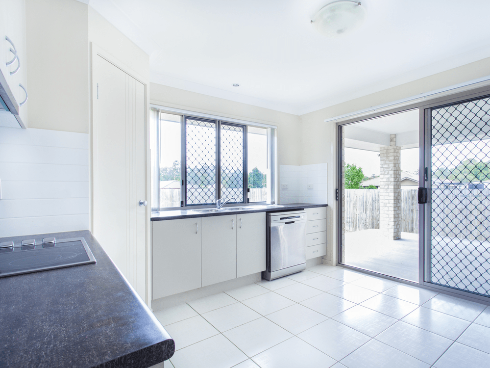 An Empty Kitchen With White Cabinets And Sliding Glass Doors — Readycut Screens & Doors in Winnellie, NT
