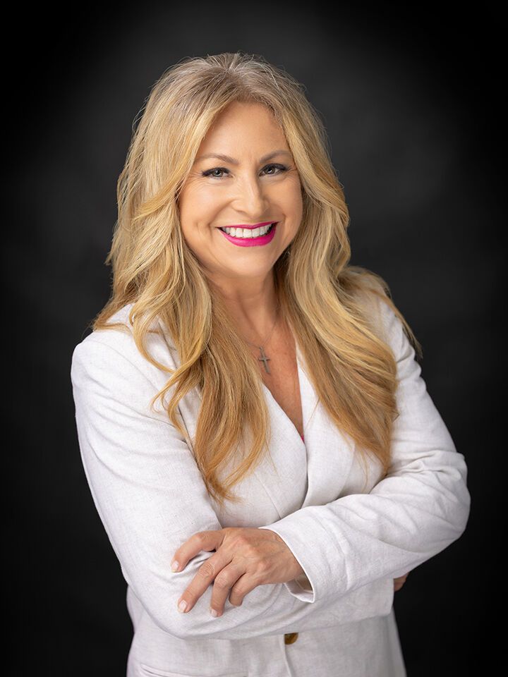 Smiling woman in a white blouse with blonde hair against a dark studio background