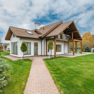 Modern white house with a brown roof, large windows, and a brick path in a green lawn