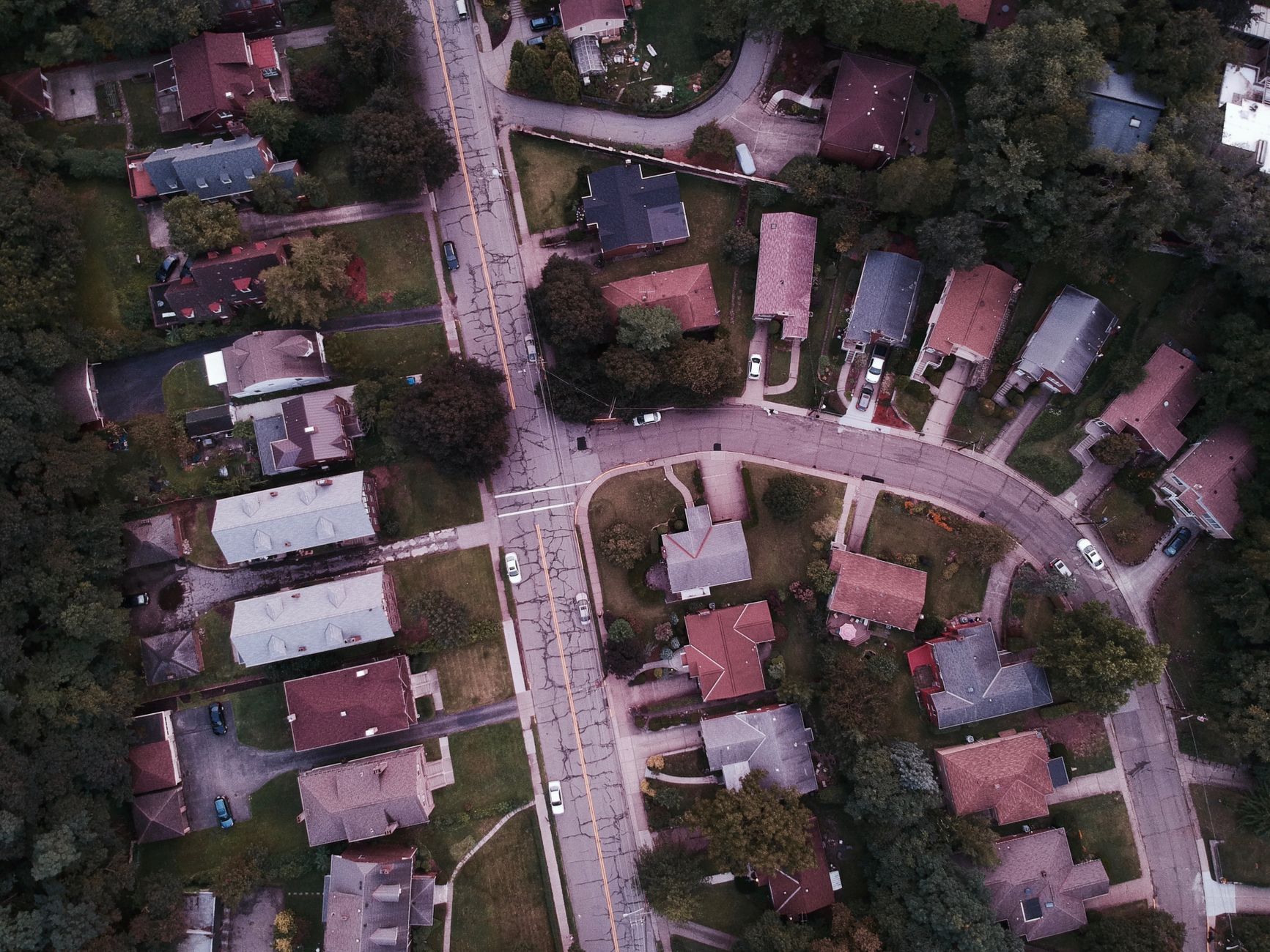 Aerial view of a suburban neighborhood with curving streets and closely packed houses surrounded by trees.