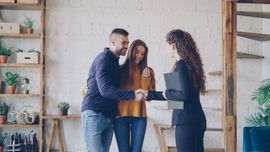 Three people discussing documents in a bright office with shelves and plants