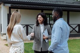 Three people talking outside a house, one holding a coffee cup and smiling.