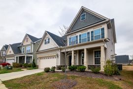 Row of suburban houses with beige siding, blue shutters, and attached garages on a cloudy day