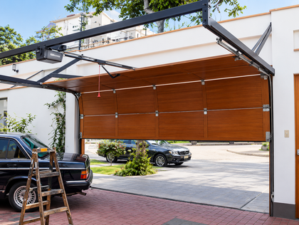 Coche negro bajo una puerta de garaje de listones de madera con una escalera al lado en una entrada de vehículos.