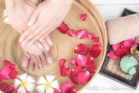 Person's hands and feet soaking in a wooden bowl with rose petals and flowers, towel and a spa treatment.