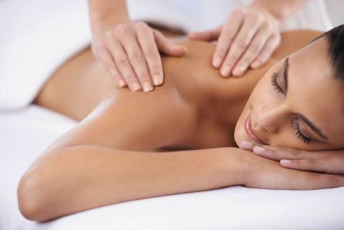 Woman receiving a back massage, lying face down on a massage table with eyes closed, hands on her shoulders.
