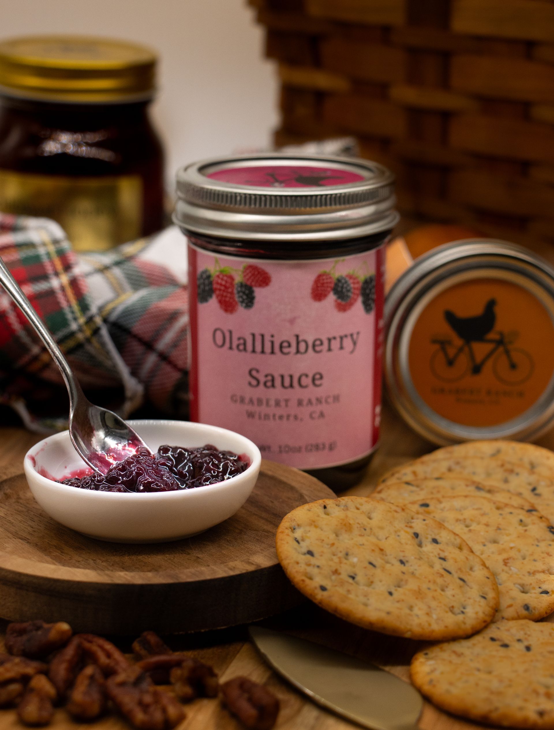 A small jar of Olallieberry sauce with a pink label featuring berry illustrations and a silver metal lid.