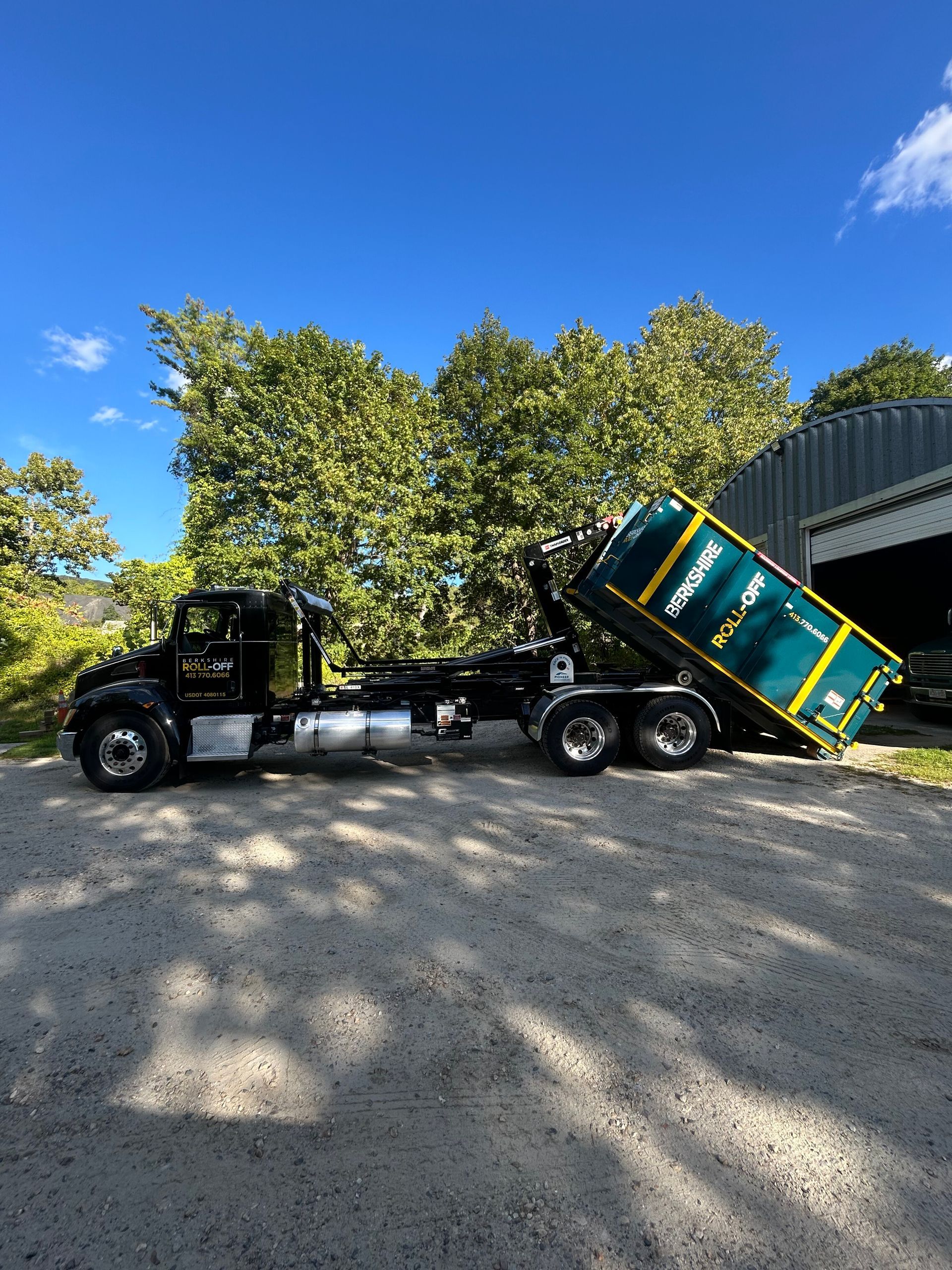 Black semi-truck hauling a green dumpster trailer on a sunny gravel lot