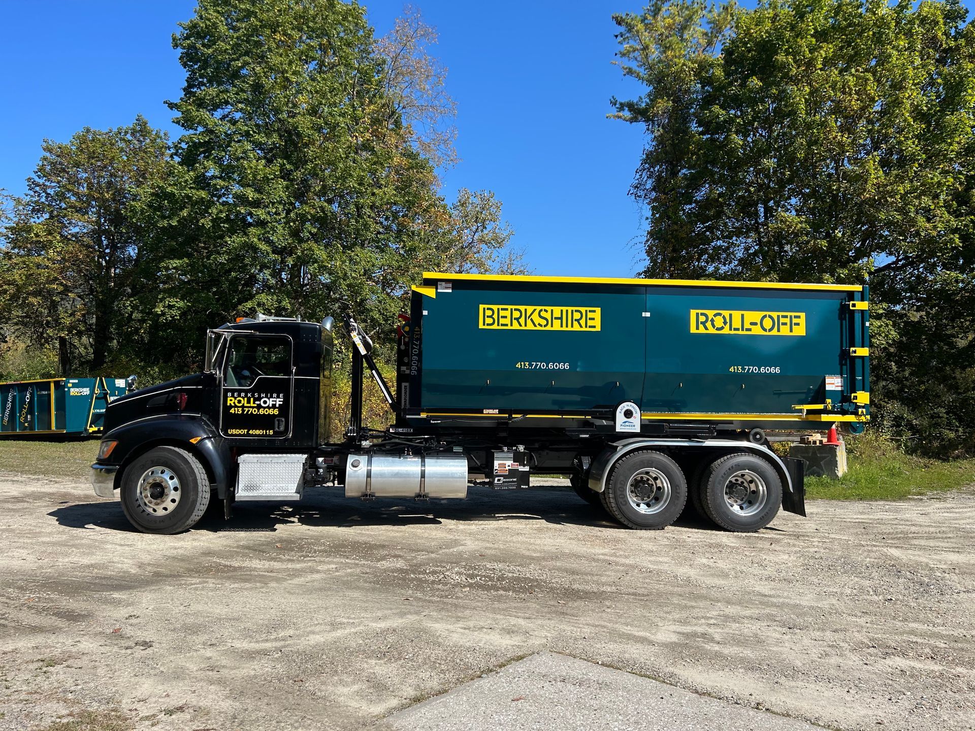 Black-and-green dump truck parked on a gravel lot with trees and blue sky behind it