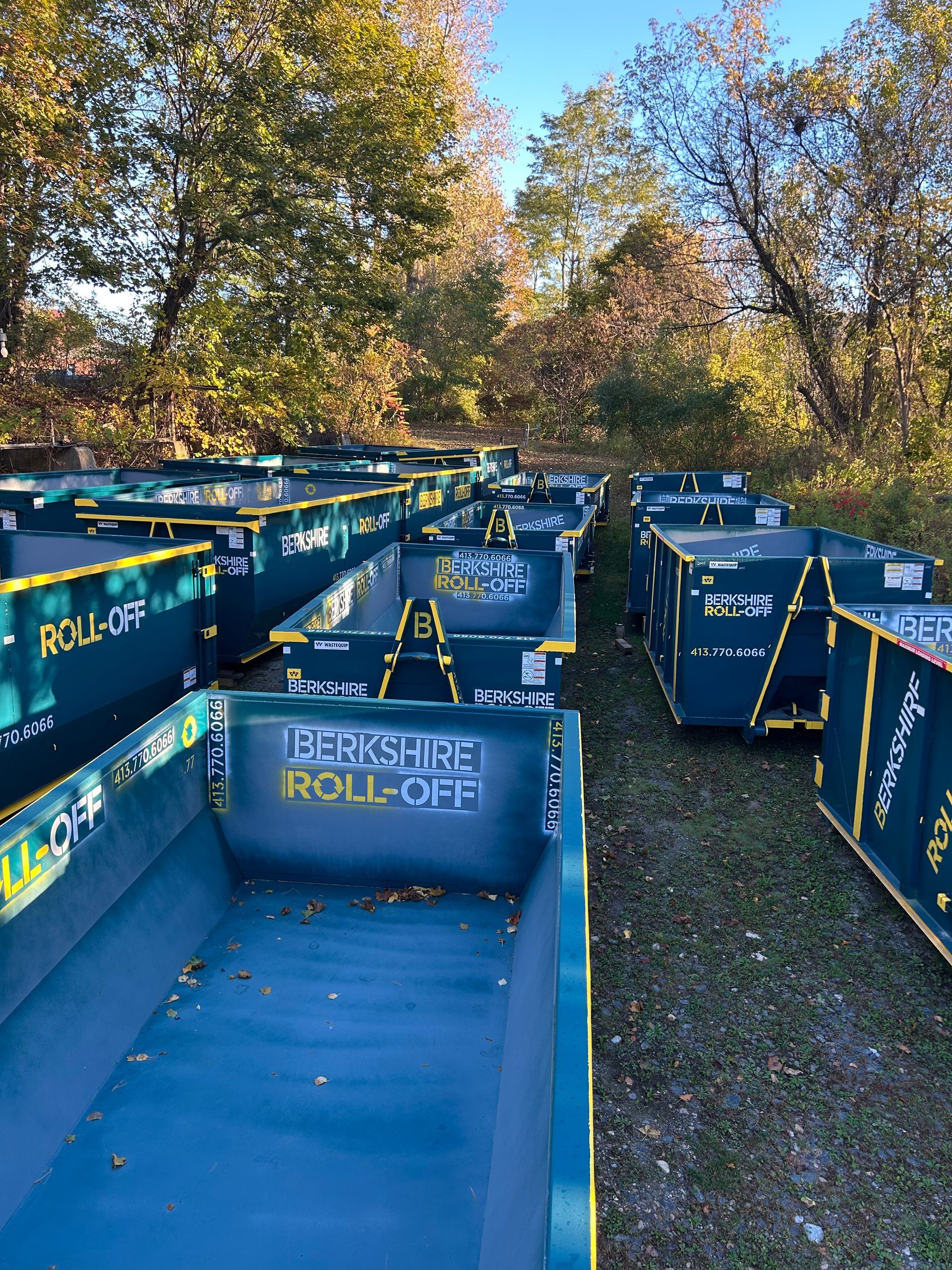 Blue “Berksher® Rail Co.” rail carts lined up outdoors on a grassy path under autumn trees.
