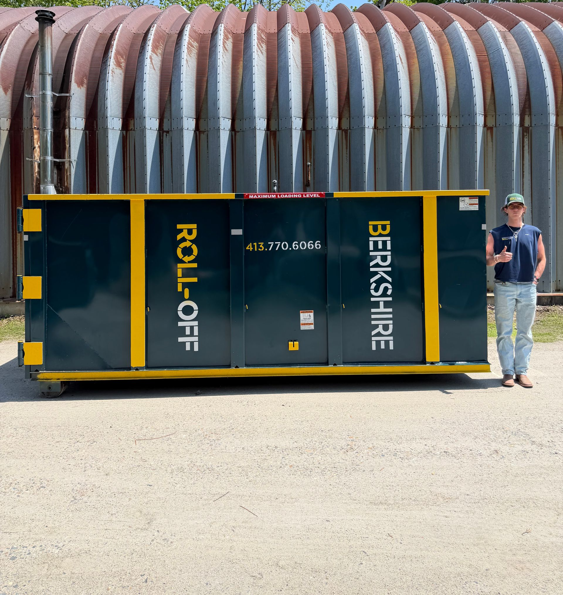 Man standing beside a dark green roll-off dumpster with yellow trim and “Berkshire” printed on the side.
