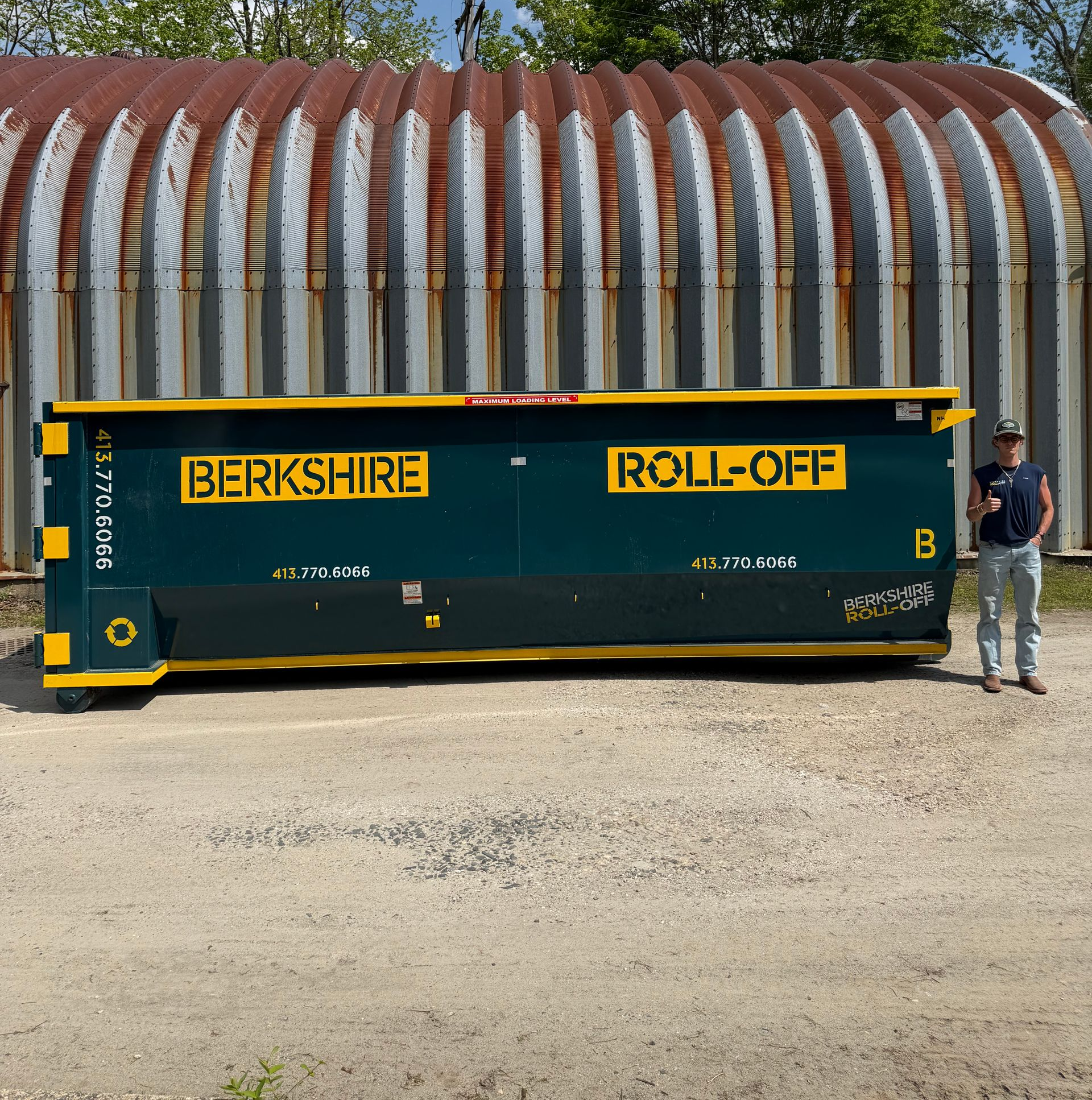 Green Berkshire roll-off dumpster with yellow lettering beside a man standing outdoors near a rusted building