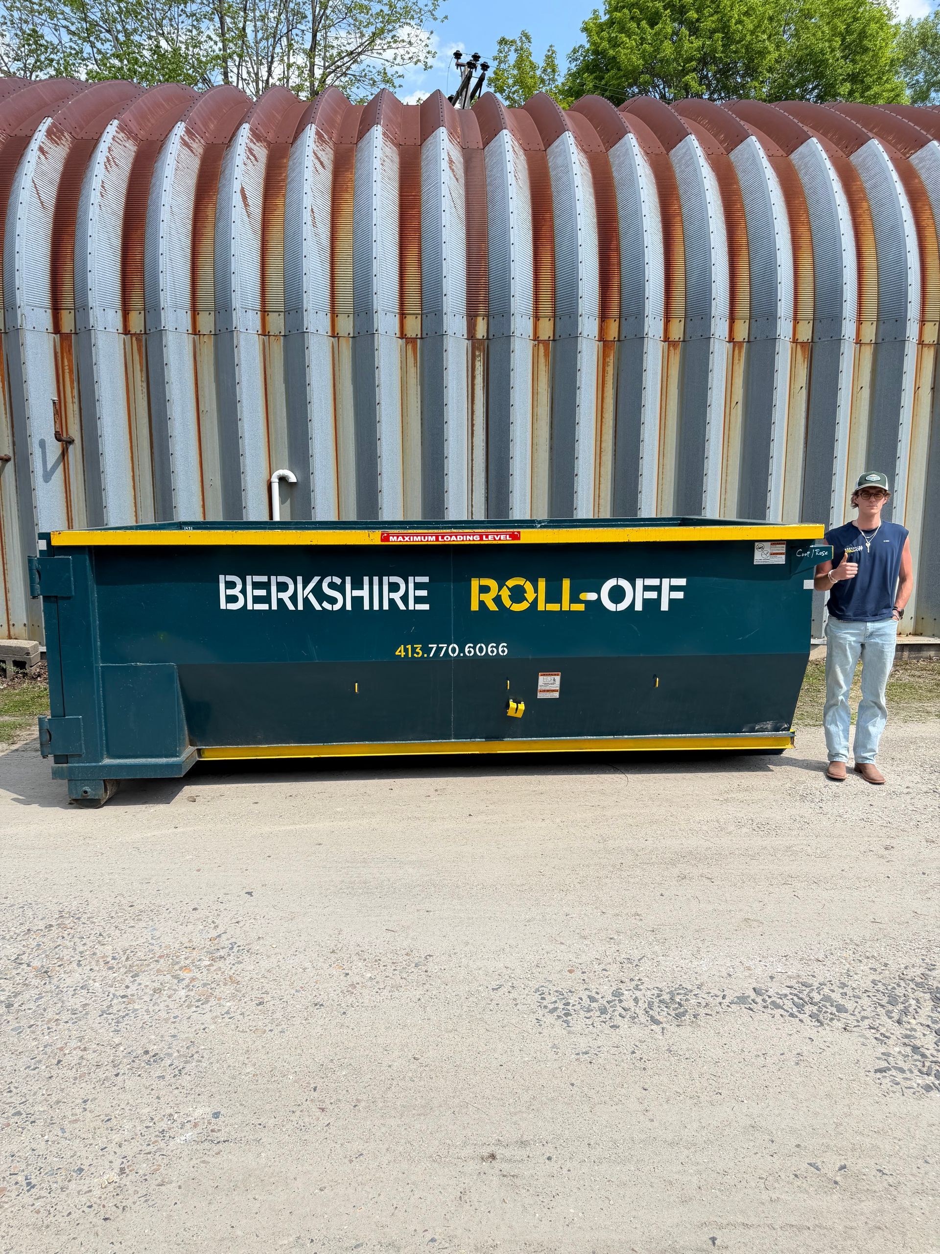 Berkshire Roll-Off dumpster in front of a rusted corrugated wall, with a man standing at the right side.