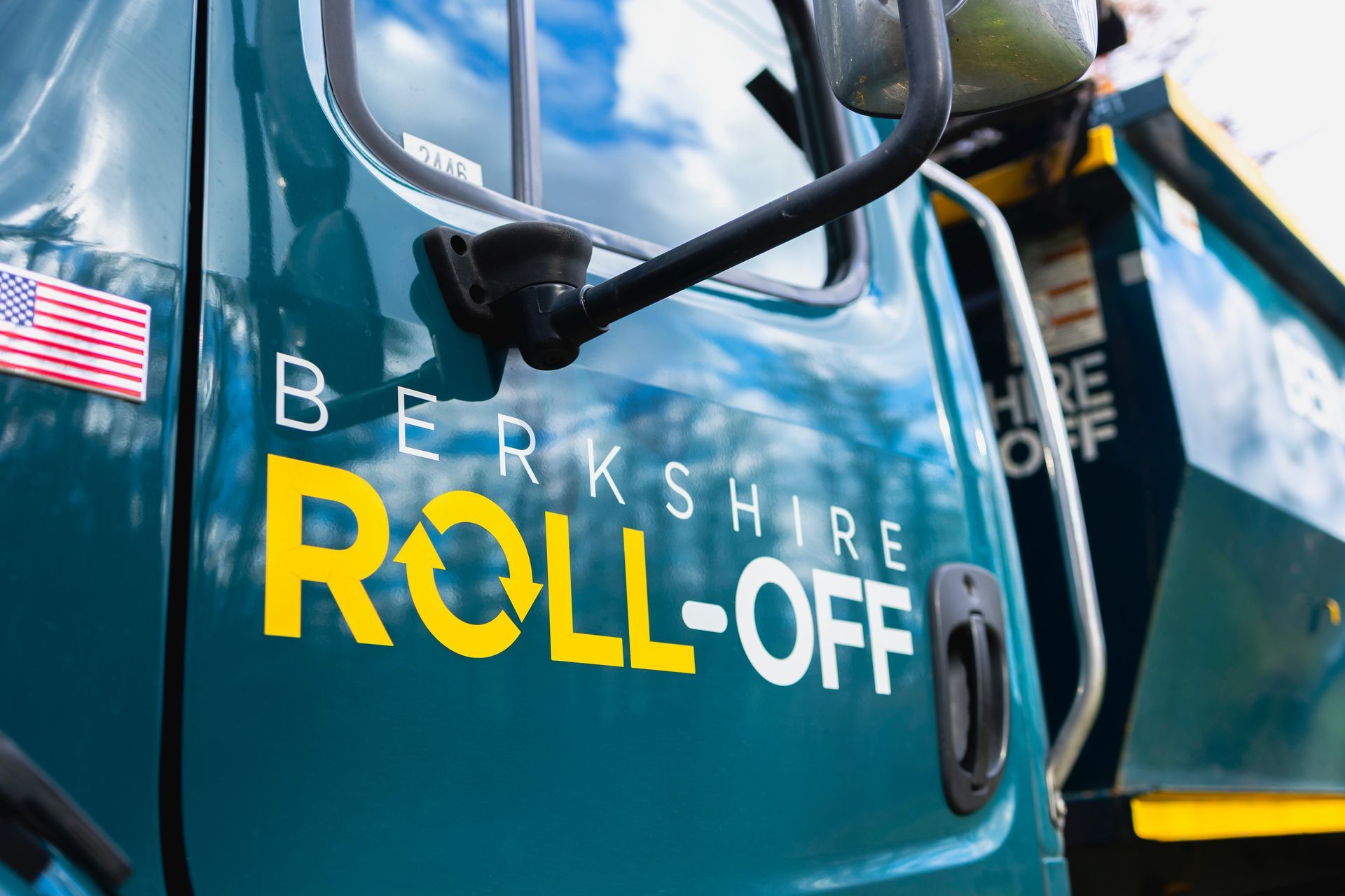 Teal Berkshire Roll-Off truck side with yellow logo and an American flag decal